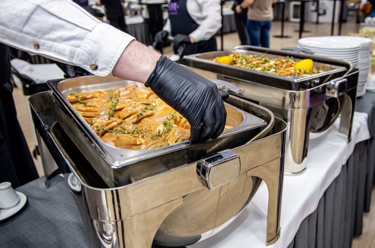 Caterer serving food from stainless steel chafing dishes at an event