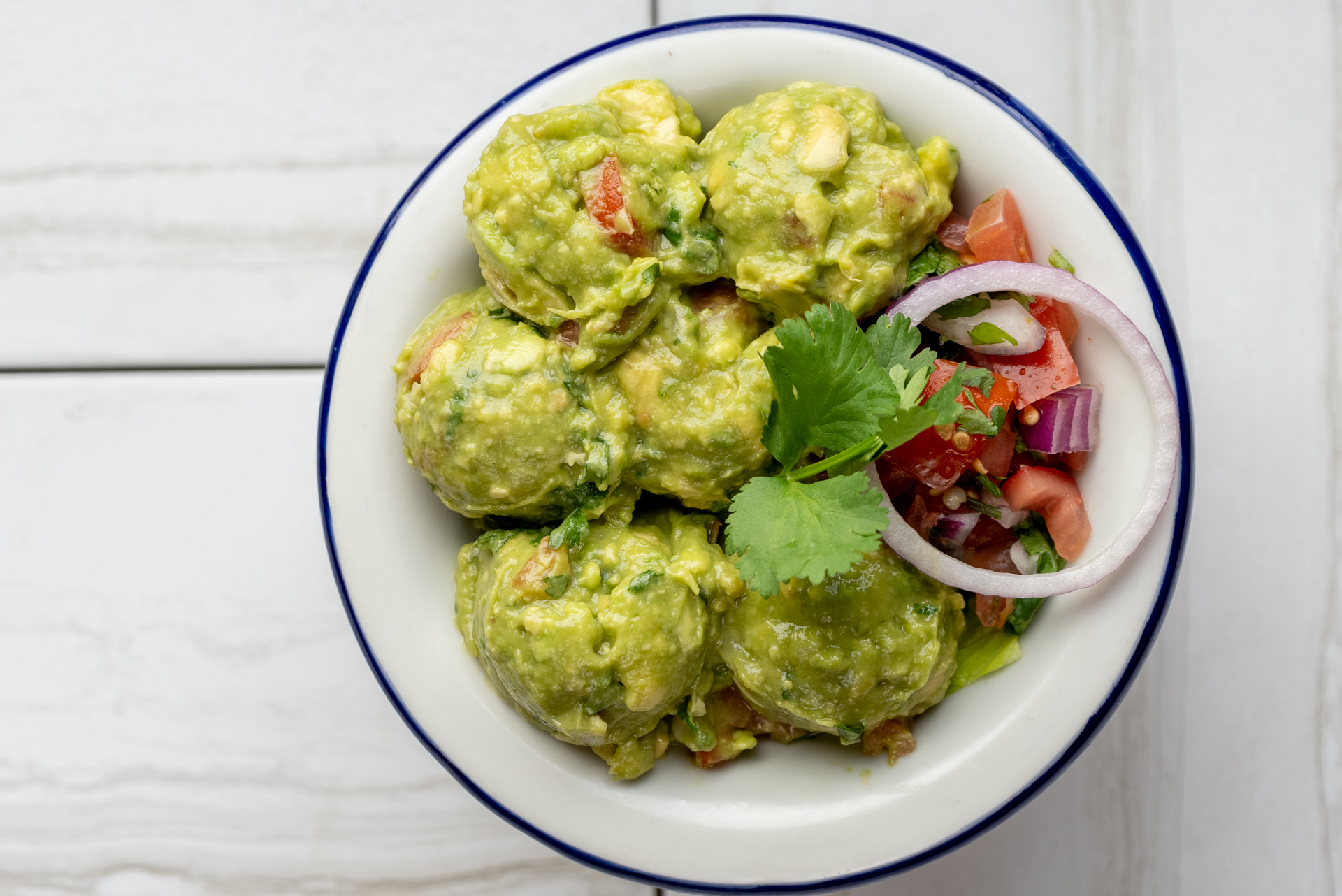 Bowl of guacamole garnished with pico de gallo and cilantro
