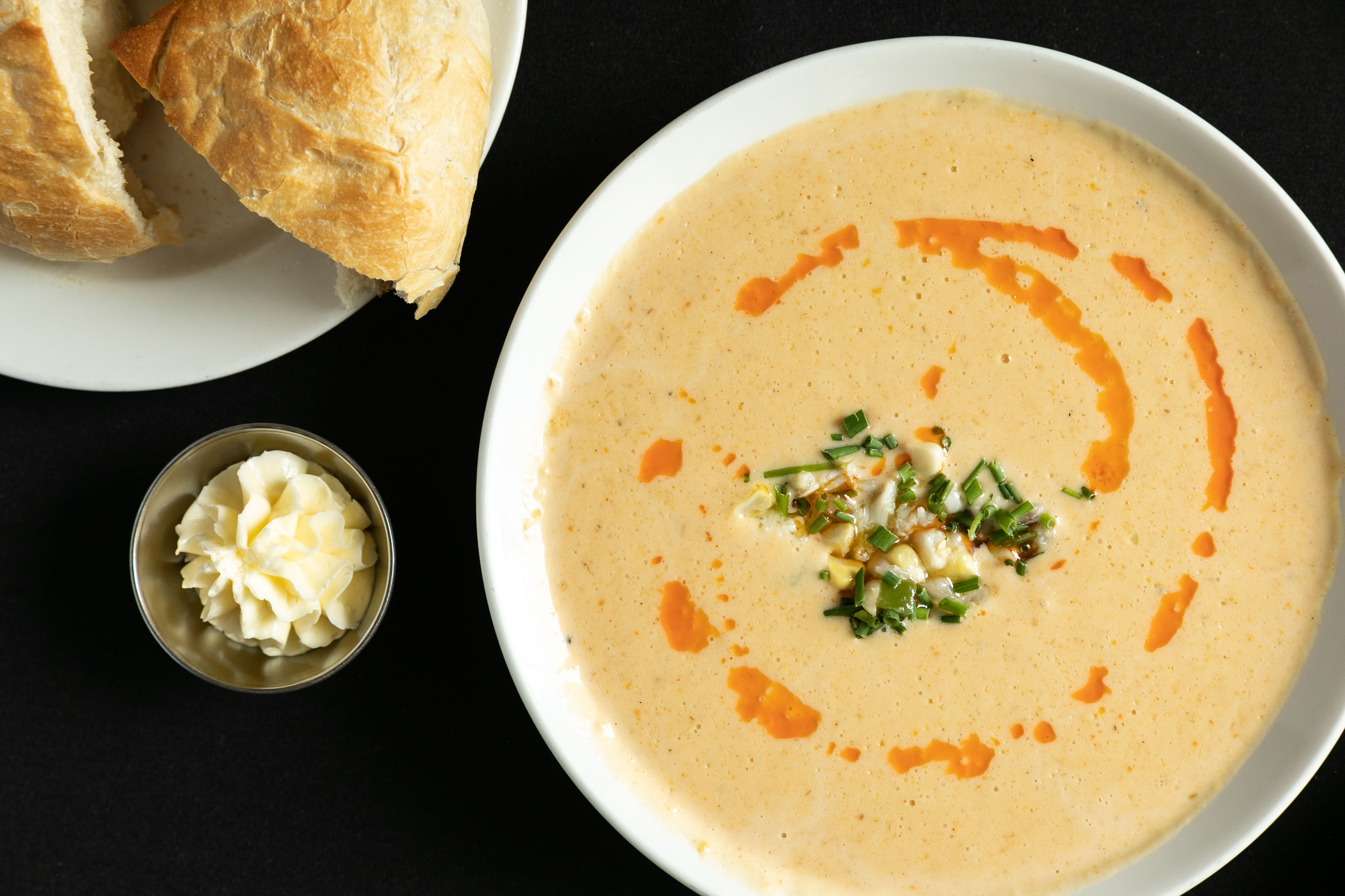 Bowl of soup garnished with chives and a swirled hot sauce drizzle