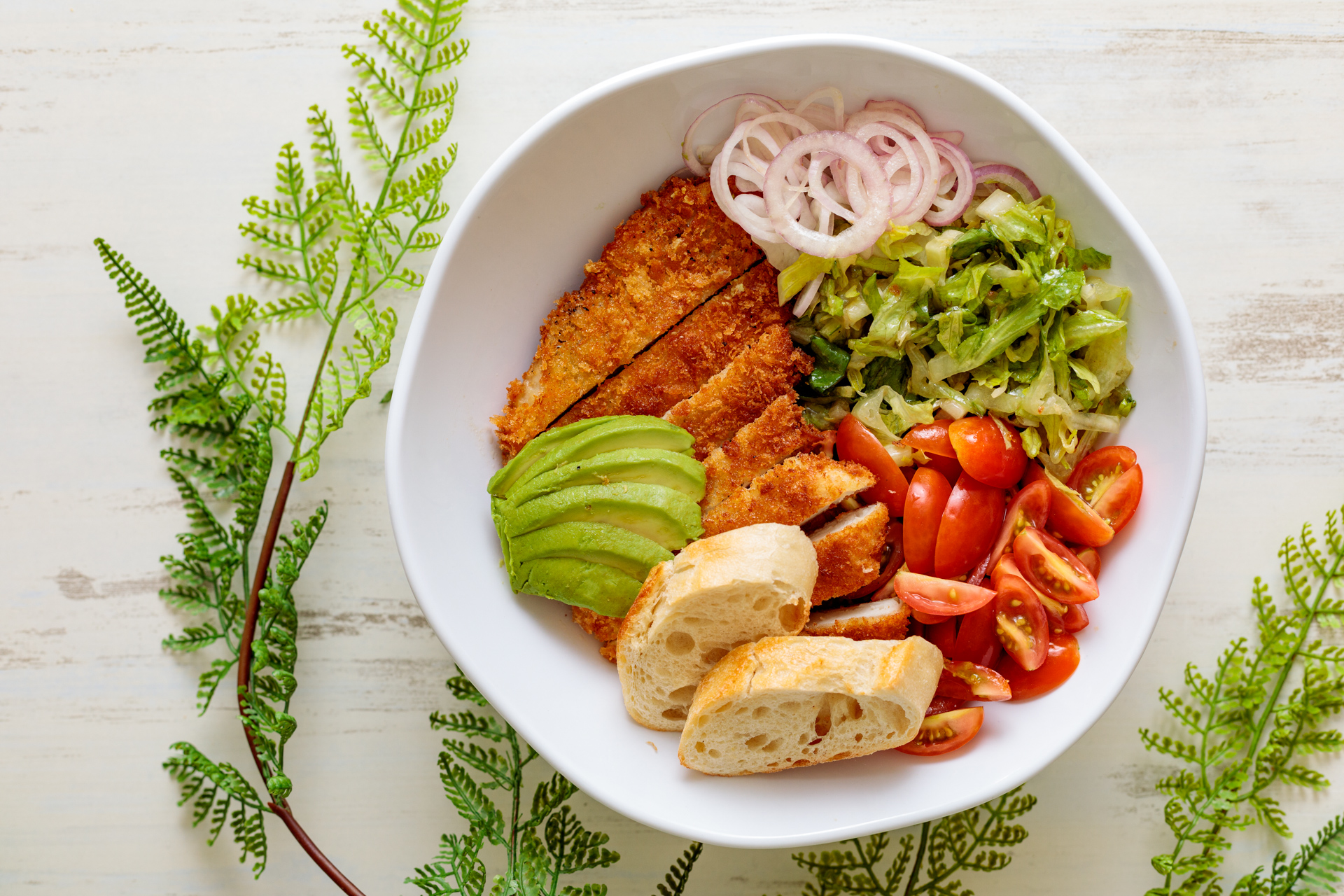 Salad bowl with breaded cutlet, avocado, tomatoes, and onions