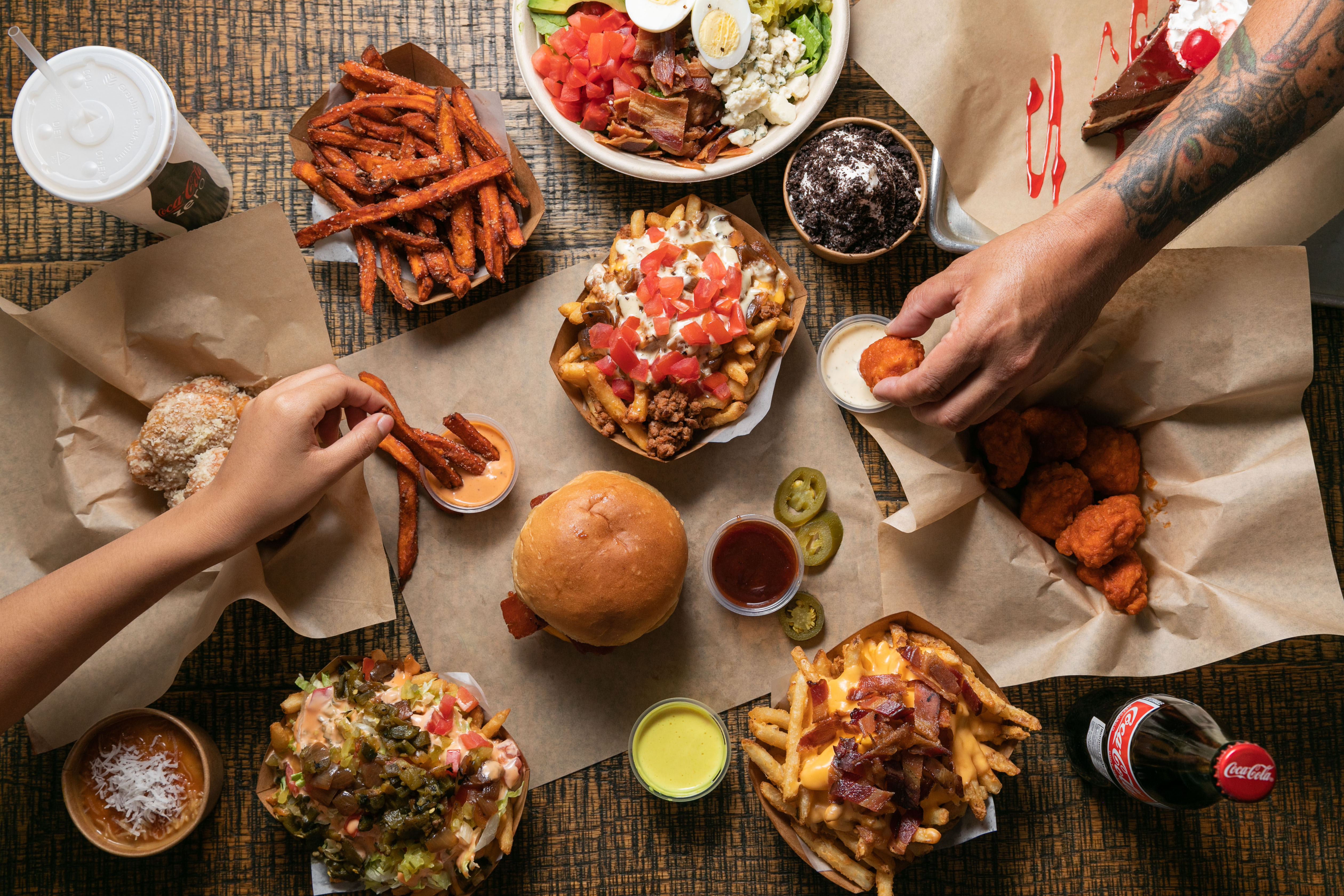 Overhead spread of burgers, loaded fries, and wings on a table