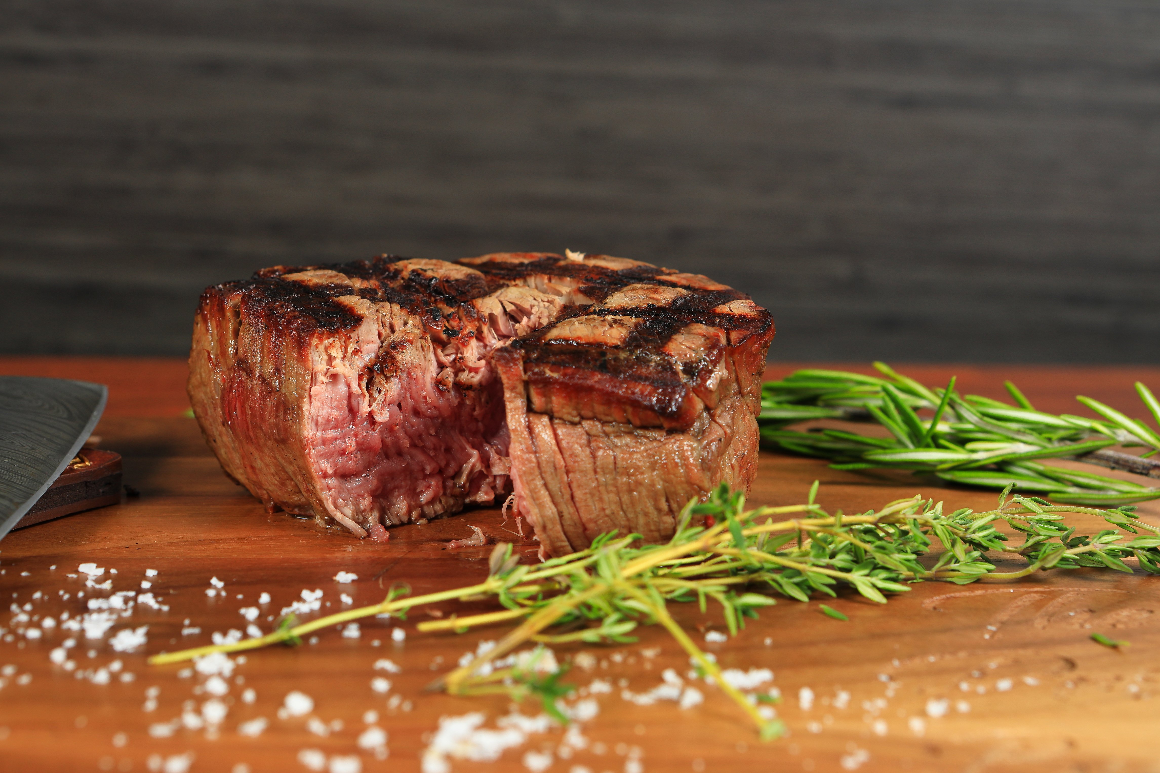 Sliced steak showing a juicy rare center next to fresh herbs