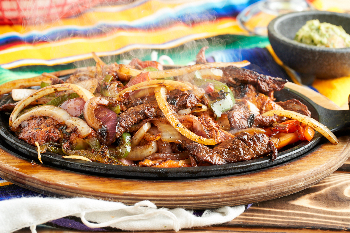 Steaming beef fajitas on a sizzling platter against a dark background