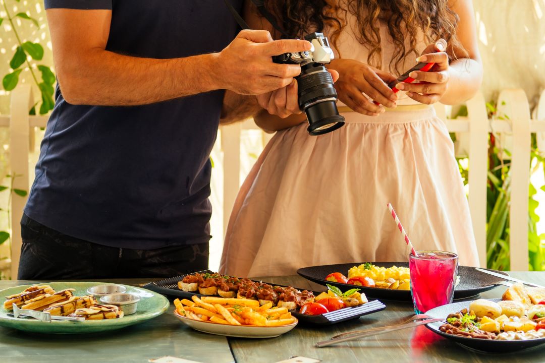 A couple photographing a table of plated dishes with a camera and phone