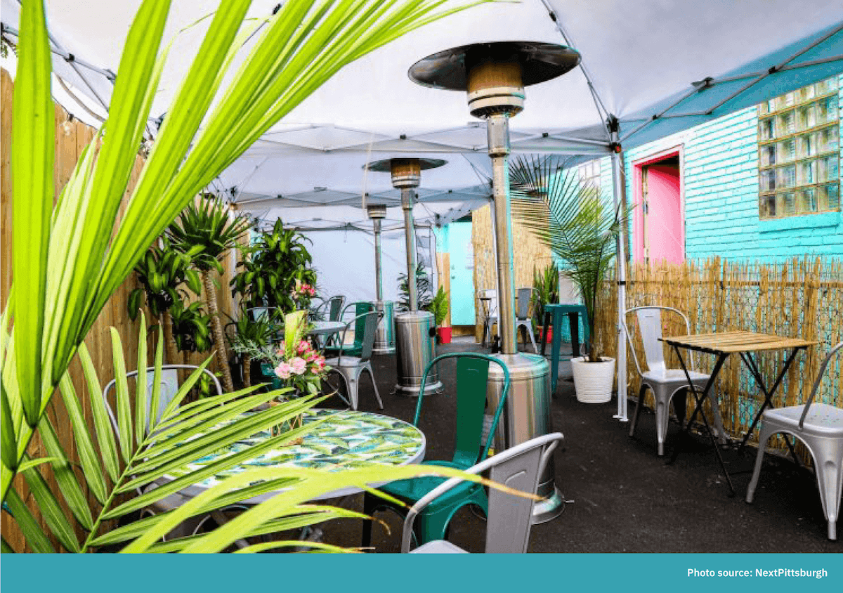 A covered patio with tented canopies, heaters, and greenery for protection from the weather