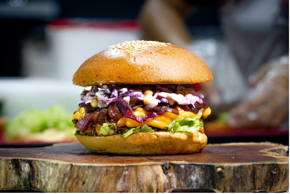 Close-up photo of a loaded burger with coleslaw and cheese