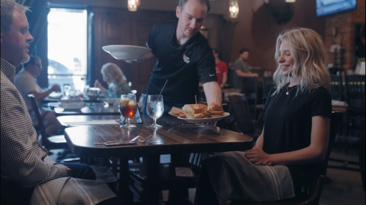 Server delivering a plate of sliders to a table of guests