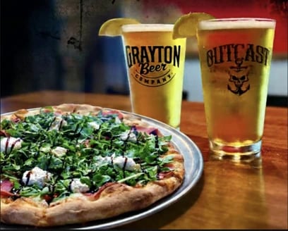 Arugula pizza on a metal tray beside two glasses of beer