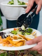Salad being served with tongs over nachos