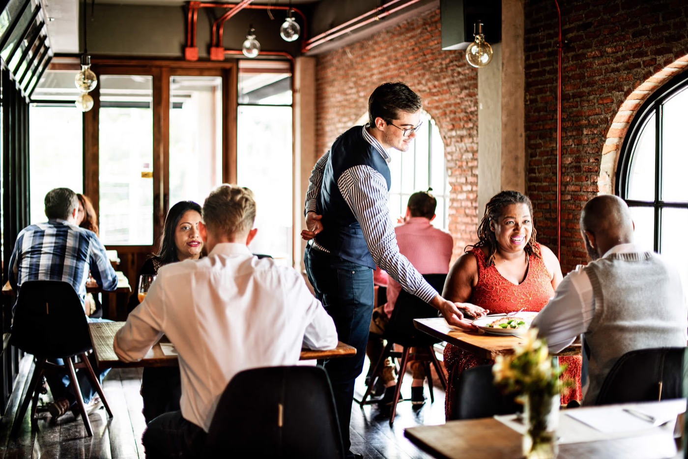 A server checking in with a full table of guests in a busy restaurant dining room