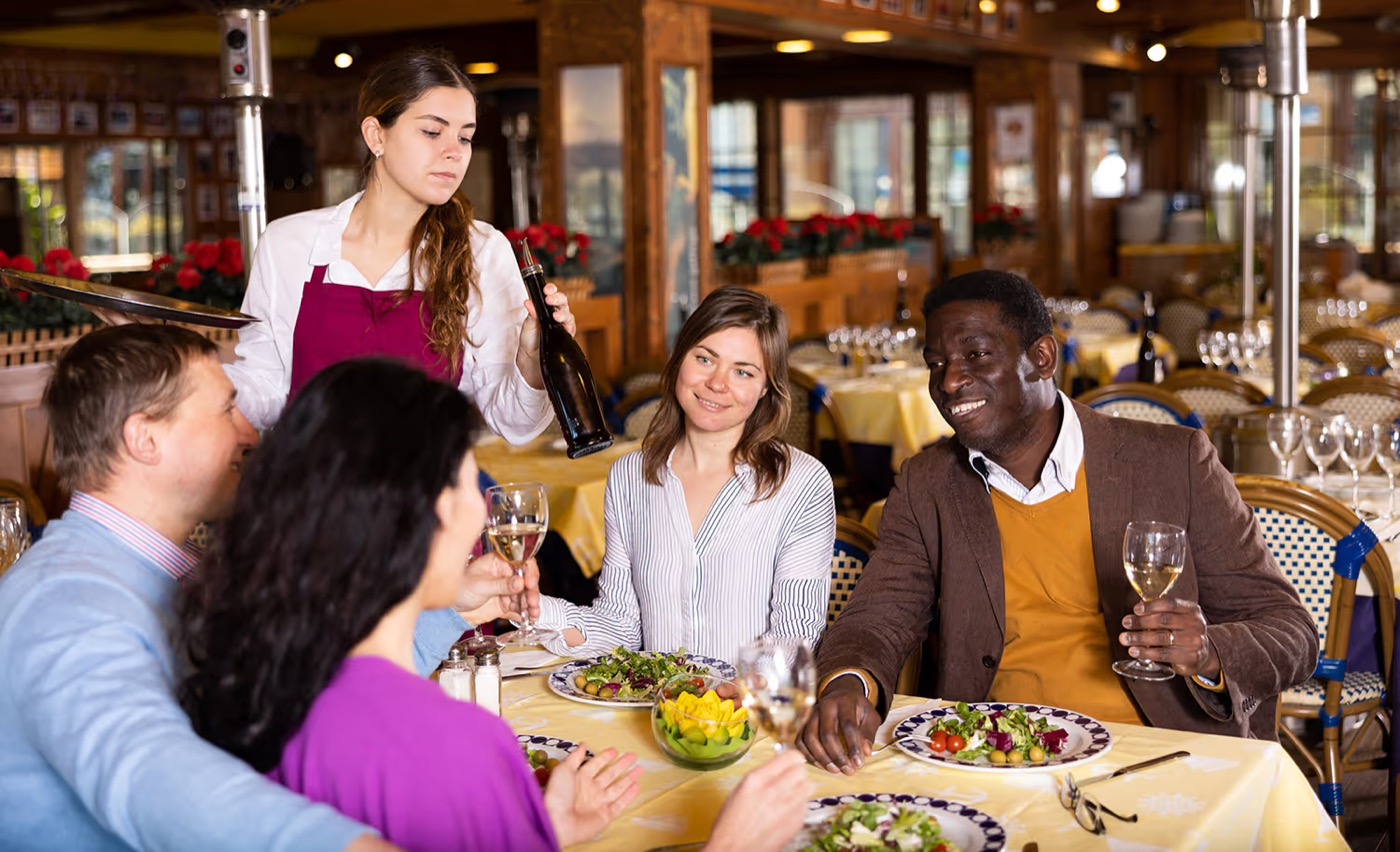 A server pouring wine for guests at a restaurant table