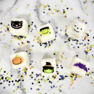 White petite fours decorated with Halloween faces — a cat, Frankenstein, ghost, pumpkin, witch hat, and bat