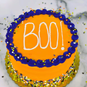 A yellow cake with blue and purple frosting, decorated with "BOO!"